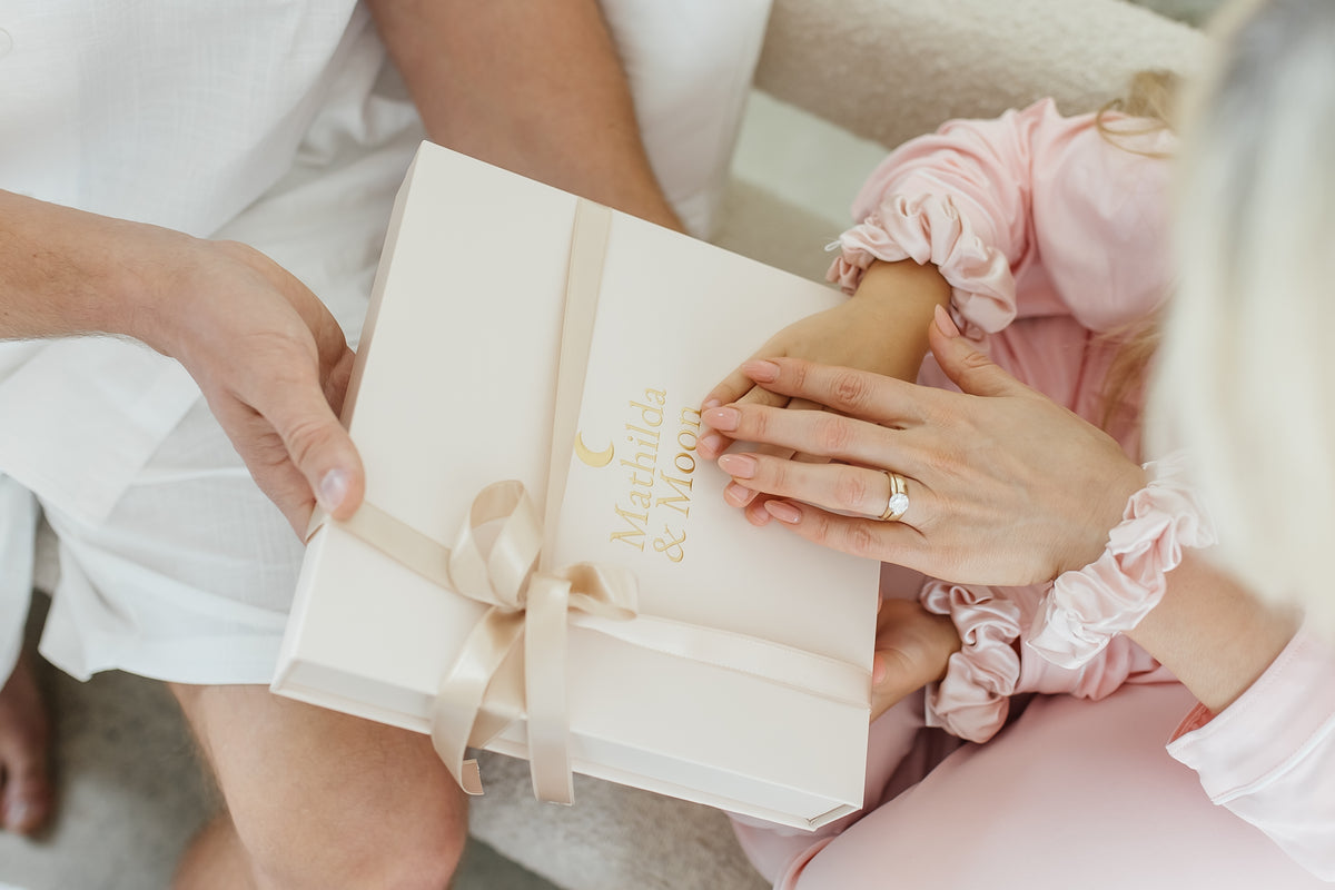 Person holding a gift box with "Mathilda & Moon" logo, surrounded by soft lighting.