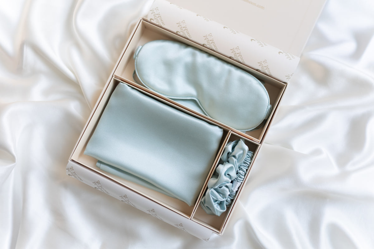Silk Set of light blue eye mask and matching pillowcase with two scrunchies in a box on a white fabric background